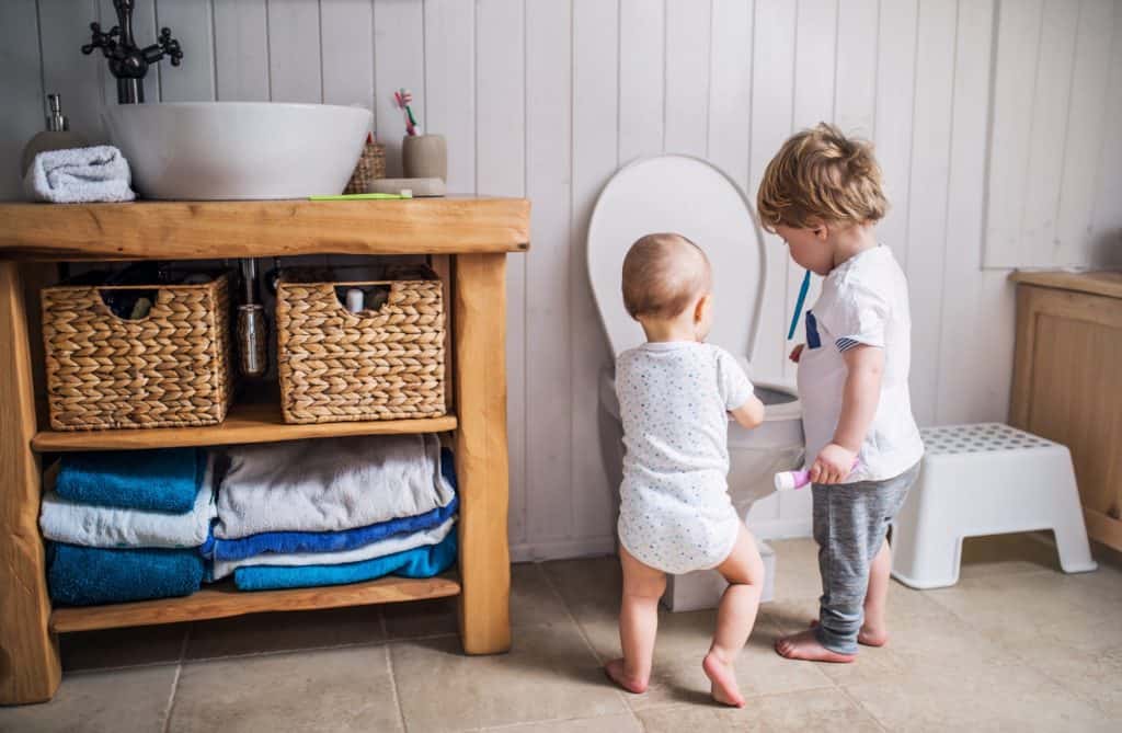 Bababarát fürdőszoba Two toddler children with toothbrush standing by the toilet in the bathroom at home.