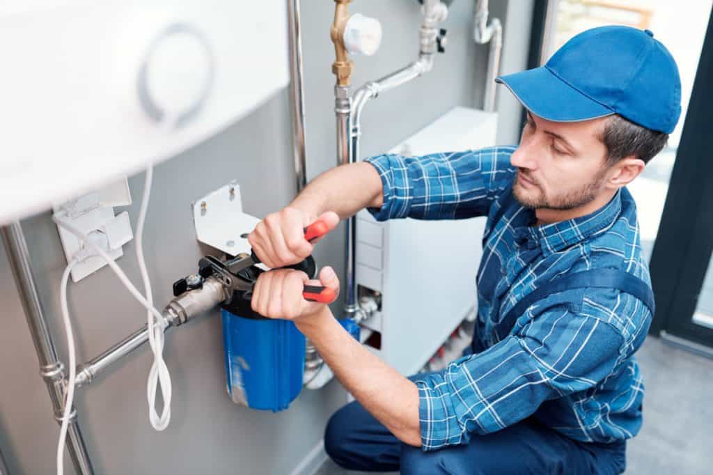 A víz minősége mellett nem mehetünk el szó nélkül, de mégis milyen forrást válasszunk? Young man in workwear using pliers while installing water filtration system