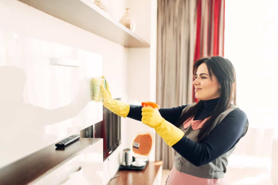 Housemaid cleans furniture with a cleaning spray