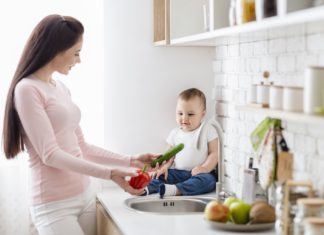 Mom with baby washing vegetables at kitchen, empty space